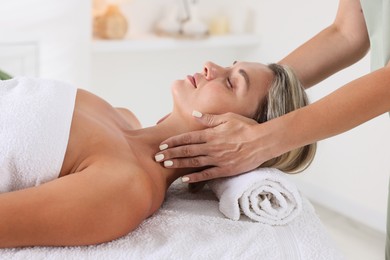 Photo of Beautiful woman receiving facial massage on couch in spa salon, closeup