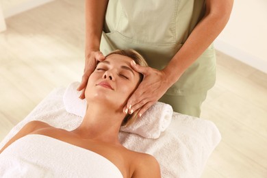 Photo of Beautiful woman receiving facial massage on couch in spa salon, closeup