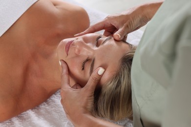 Photo of Beautiful woman receiving facial massage on couch indoors, closeup