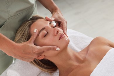 Photo of Beautiful woman receiving facial massage on couch indoors, closeup