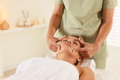 Photo of Beautiful woman receiving facial massage on couch indoors, closeup