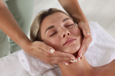 Photo of Beautiful woman receiving facial massage on couch indoors, closeup
