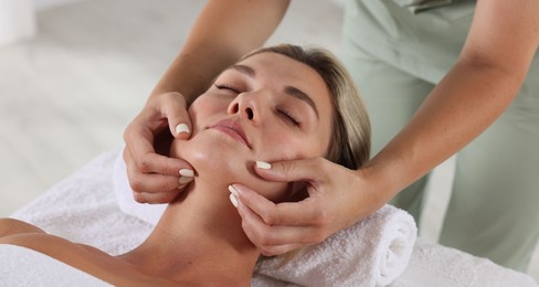 Photo of Beautiful woman receiving facial massage on couch indoors, closeup