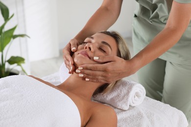 Photo of Beautiful woman receiving facial massage on couch indoors, closeup