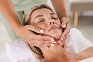 Photo of Beautiful woman receiving facial massage on couch indoors, closeup