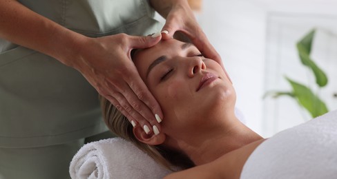 Photo of Beautiful woman receiving facial massage indoors, closeup