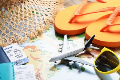 Photo of Time for summer vacation. Passports, flight tickets, toy plane and beach accessories on world map, closeup