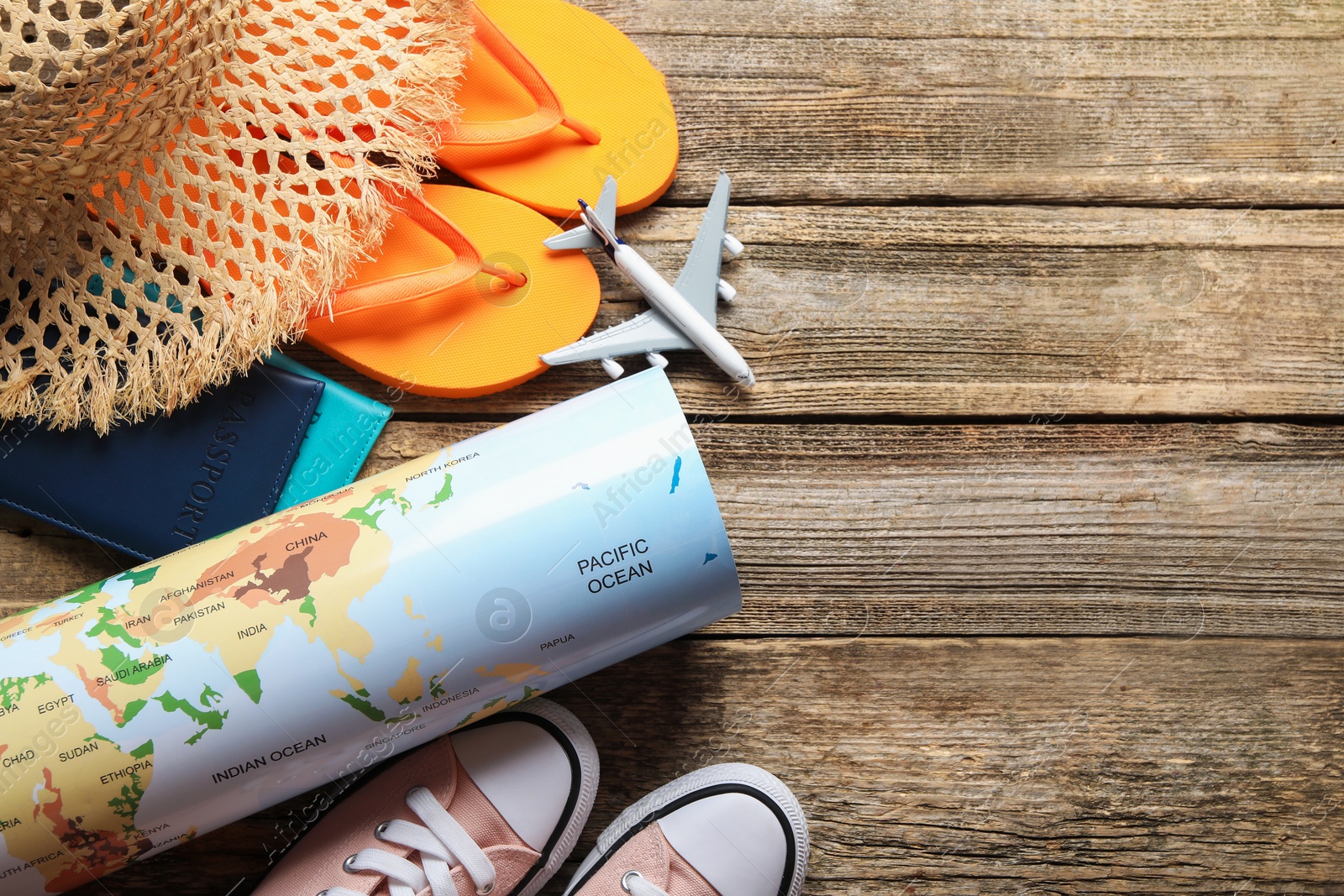 Photo of Time for summer vacation. World map, passports, toy plane, shoes and beach accessories on wooden table, flat lay. Space for text