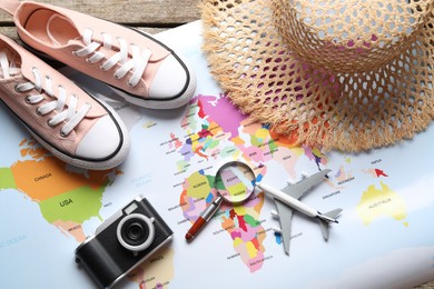 Photo of Time for summer vacation. World map, magnifying glass, toy plane, shoes, camera and straw hat on wooden table, flat lay