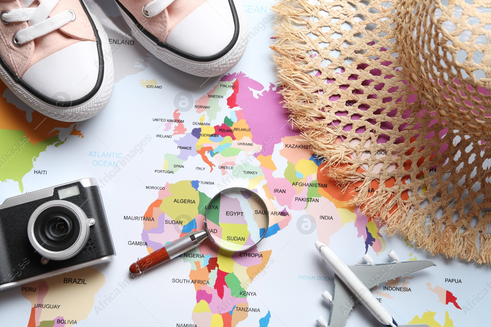 Photo of Time for summer vacation. Magnifying glass, toy plane, shoes, camera and straw hat on world map, flat lay