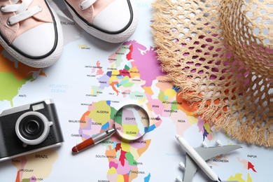 Photo of Time for summer vacation. Magnifying glass, toy plane, shoes, camera and straw hat on world map, flat lay