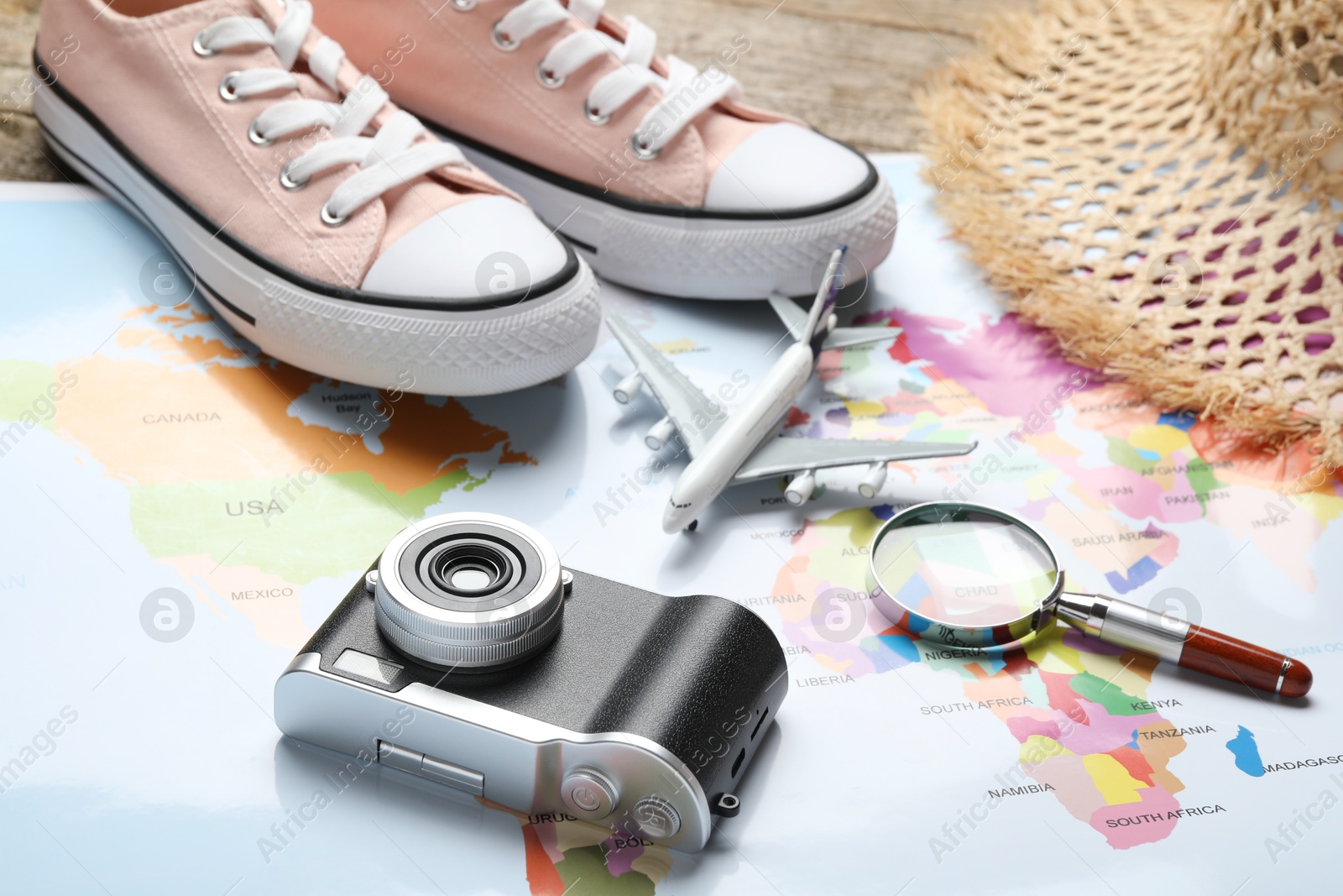 Photo of Time for summer vacation. World map, magnifying glass, toy plane, shoes, camera and straw hat on table, closeup