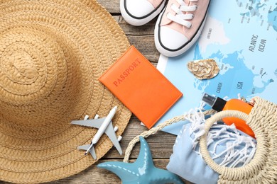 Photo of Time for summer vacation. World map, passport, toy plane, shoes, magnifying glass and beach accessories on wooden table, flat lay