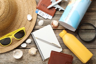 Photo of Time for summer vacation. Stationery, passport, flight tickets, toy plane, world map, purse and beach accessories on wooden table, flat lay
