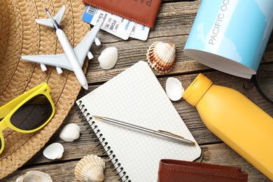 Photo of Time for summer vacation. Stationery, passport, flight tickets, toy plane, world map, purse and beach accessories on wooden table, flat lay