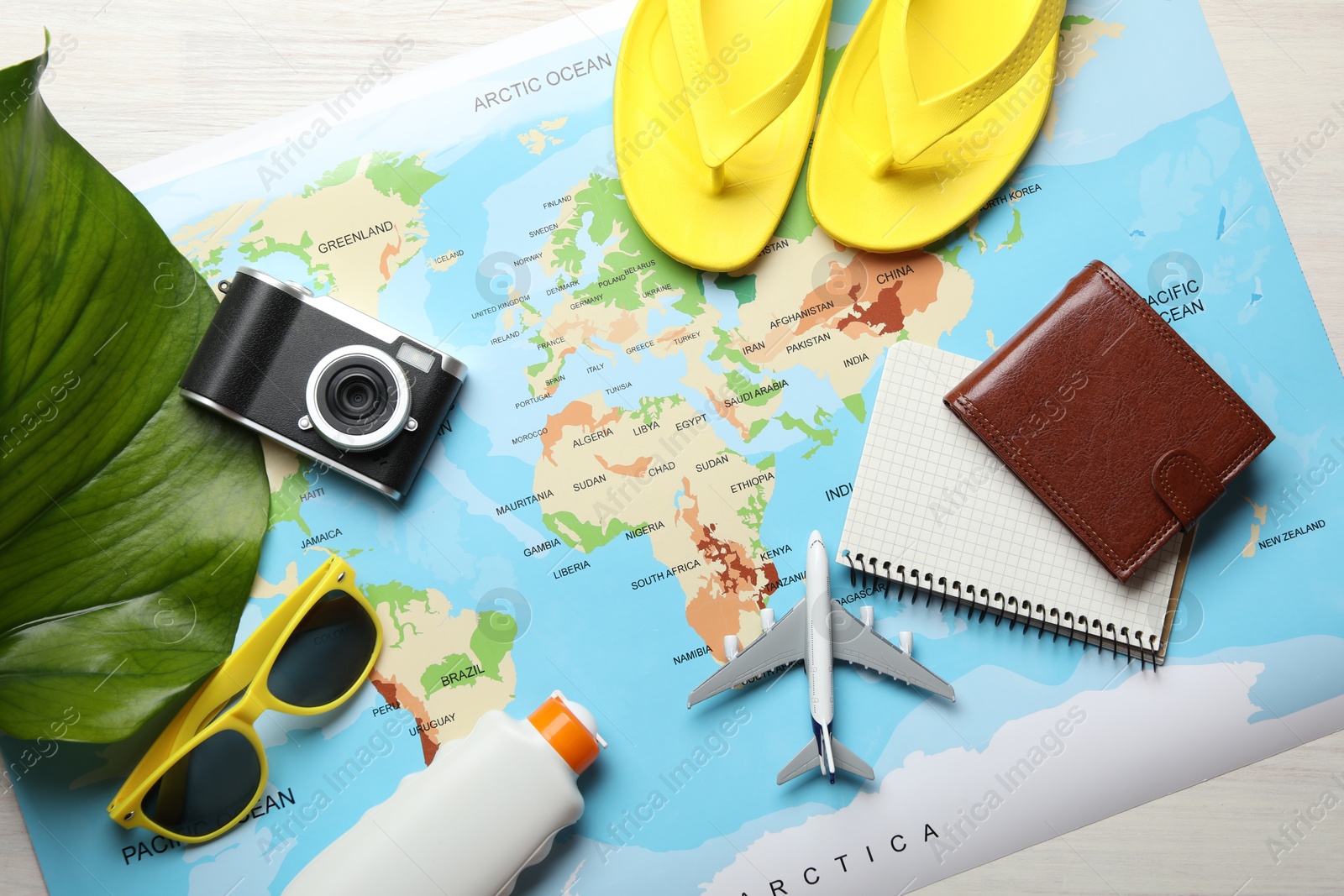 Photo of Time for summer vacation. World map, toy plane, camera, purse, green leaf and beach accessories on light wooden table, flat lay