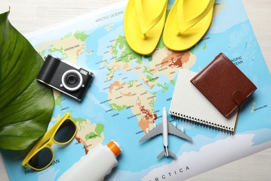 Photo of Time for summer vacation. World map, toy plane, camera, purse, green leaf and beach accessories on light wooden table, flat lay