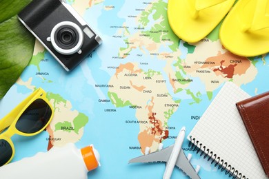 Photo of Time for summer vacation. Toy plane, camera, notebook, green leaf and beach accessories on world map, flat lay