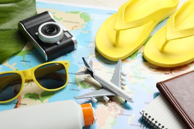 Photo of Time for summer vacation. Toy plane, camera, notebook, green leaf and beach accessories on world map, closeup
