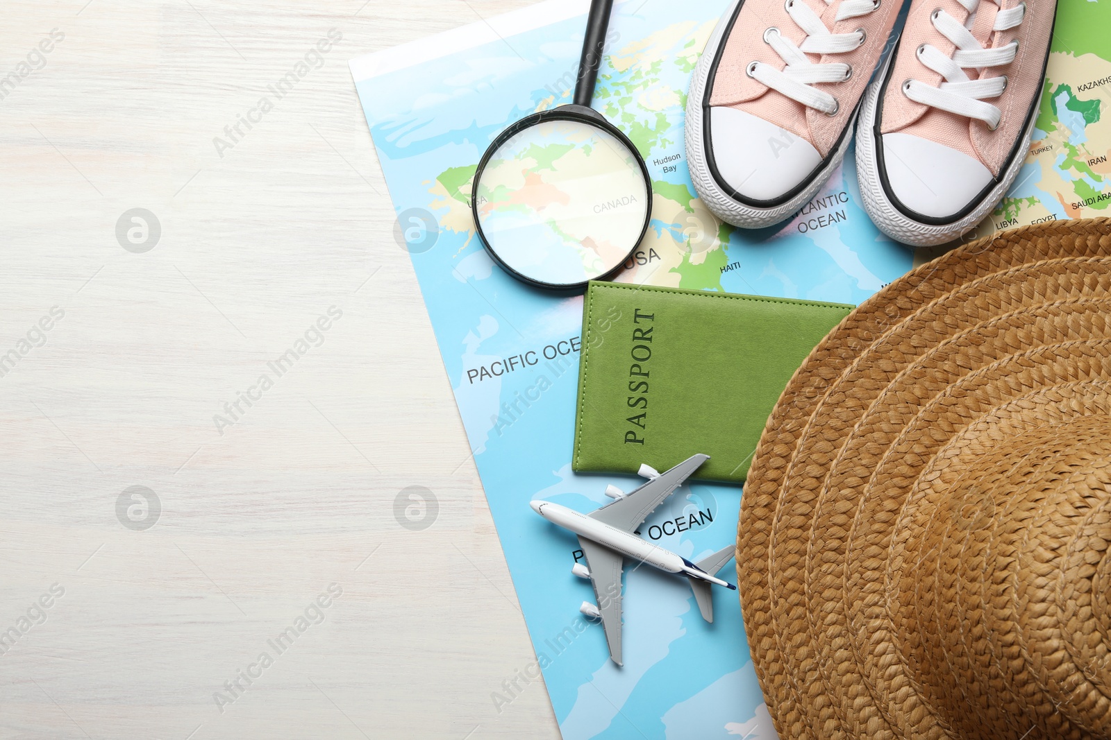 Photo of Time for summer vacation. World map, toy plane, passport, magnifying glass, shoes and straw hat on light wooden table, flat lay. Space for text