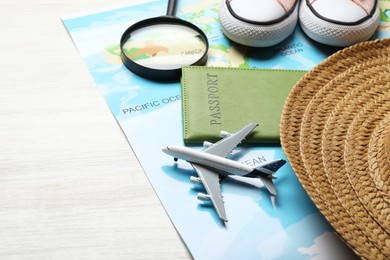 Photo of Time for summer vacation. World map, toy plane, passport, magnifying glass, shoes and straw hat on light wooden table, closeup. Space for text