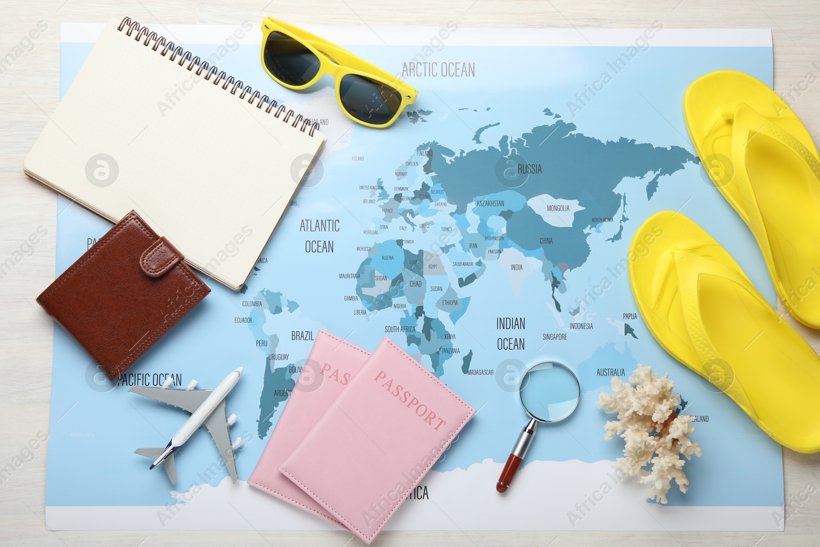 Photo of Time for summer vacation. World map, toy plane, passports, purse, magnifying glass, notebook and beach accessories on light wooden table, flat lay