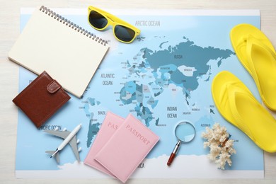 Photo of Time for summer vacation. World map, toy plane, passports, purse, magnifying glass, notebook and beach accessories on light wooden table, flat lay