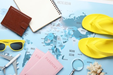 Photo of Time for summer vacation. Toy plane, passports, purse, magnifying glass, notebook and beach accessories on world map, flat lay