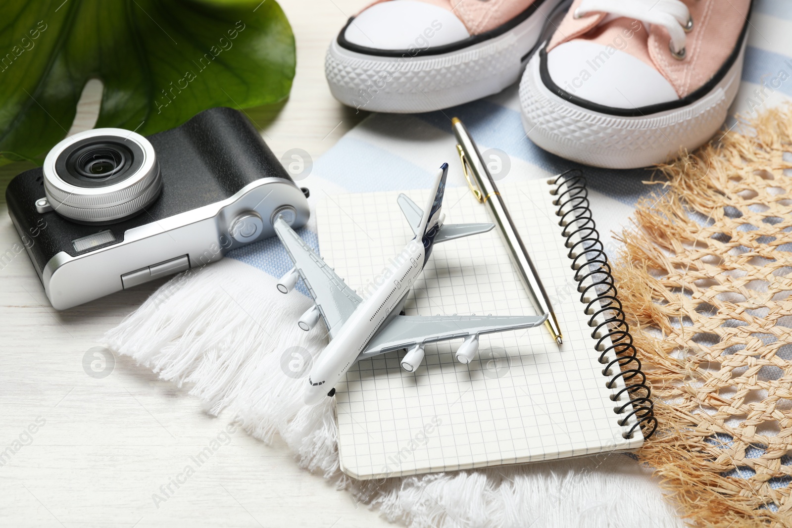 Photo of Time for summer vacation. Toy plane, stationery, shoes, camera, green leaf and beach accessories on light wooden table, closeup