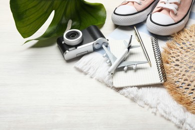 Photo of Time for summer vacation. Toy plane, stationery, shoes, camera, green leaf and beach accessories on light wooden table, closeup. Space for text