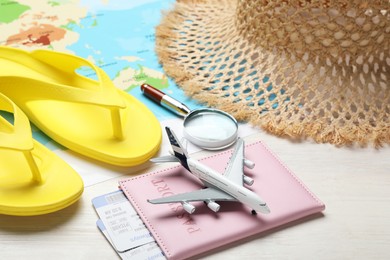 Photo of Time for summer vacation. World map, toy plane, passport, flight tickets, magnifying glass and beach accessories on light wooden table, closeup
