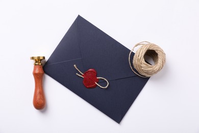 Photo of Envelope with wax seal, twine and stamp on white background, flat lay