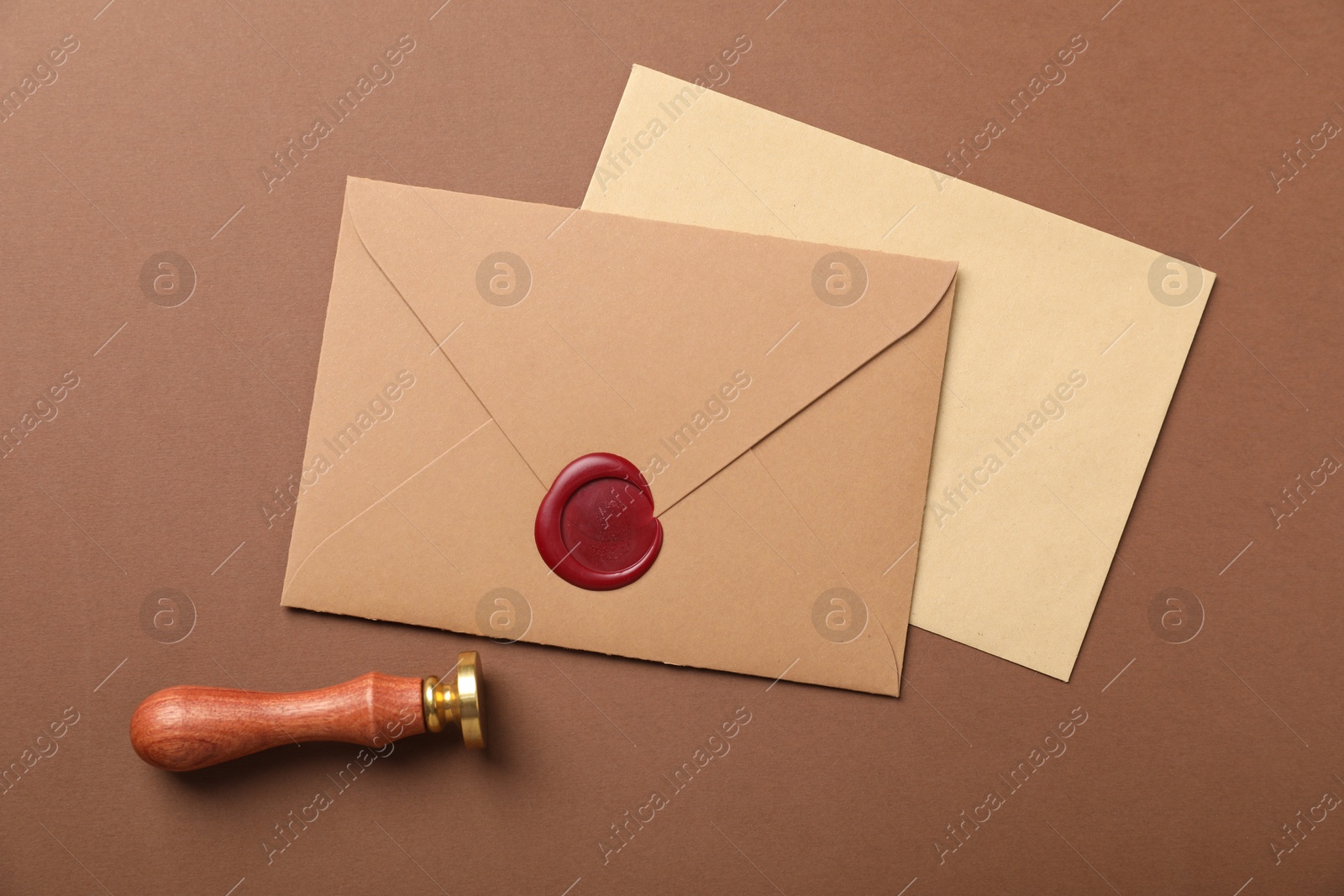 Envelopes with wax seal and stamp on brown background, flat lay Photo of Envelopes with wax seal and stamp on brown background, flat lay