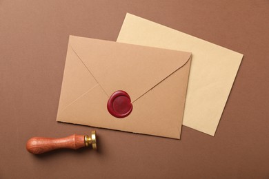 Photo of Envelopes with wax seal and stamp on brown background, flat lay