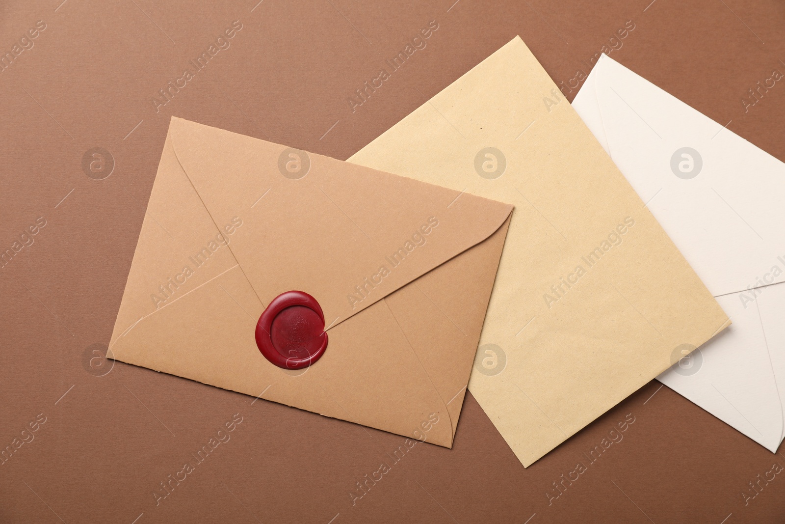 Envelopes with wax seal on brown background, flat lay Photo of Envelopes with wax seal on brown background, flat lay
