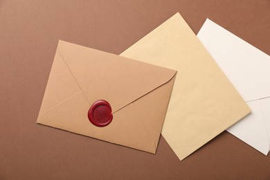 Photo of Envelopes with wax seal on brown background, flat lay