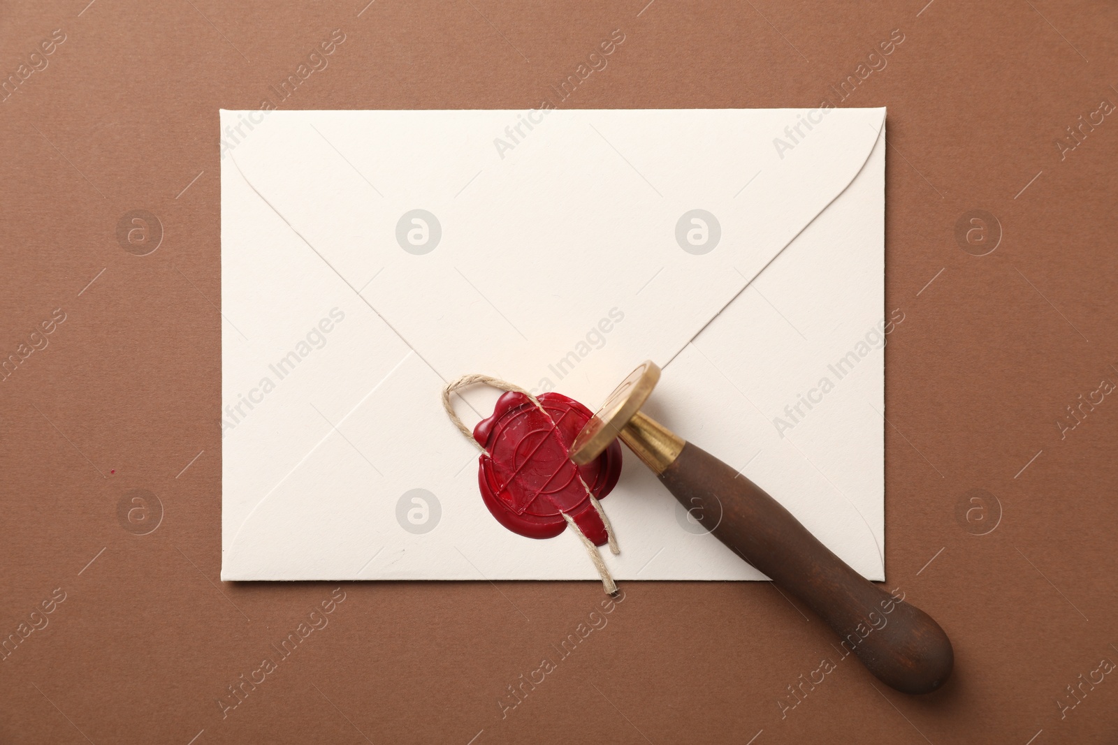Envelope with wax seal, twine and stamp on brown background, top view Photo of Envelope with wax seal, twine and stamp on brown background, top view