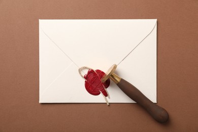 Photo of Envelope with wax seal, twine and stamp on brown background, top view