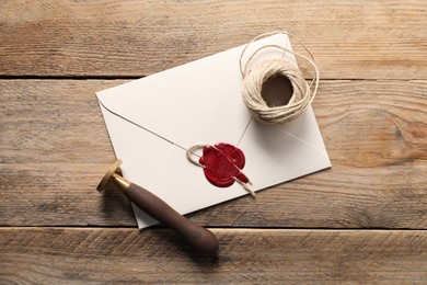 Photo of Envelope with wax seal, twine and stamp on wooden table, flat lay