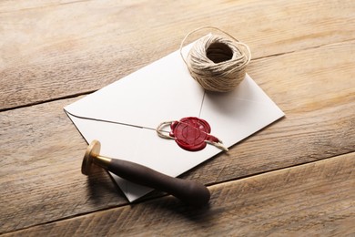 Photo of Envelope with wax seal, twine and stamp on wooden table