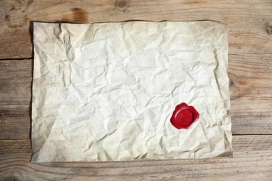 Photo of Crumpled paper with wax seal on wooden table, top view