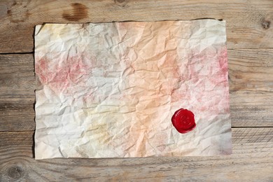 Photo of Crumpled paper with wax seal on wooden table, top view