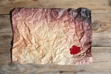 Photo of Crumpled paper with wax seal on wooden table, top view
