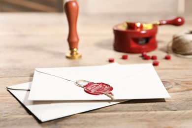 Photo of Envelope with wax seal, twine and stamp on wooden table, closeup