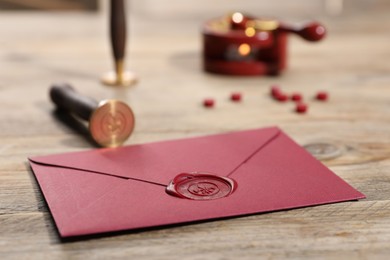 Photo of Envelope with wax seal and stamp on wooden table, closeup