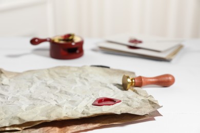 Photo of Crumpled papers with wax seal and stamp on white wooden table, closeup
