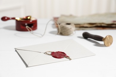 Photo of Envelope with wax seal and stamp on white wooden table, closeup
