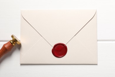 Photo of Envelope with wax seal and stamp on white wooden table, top view