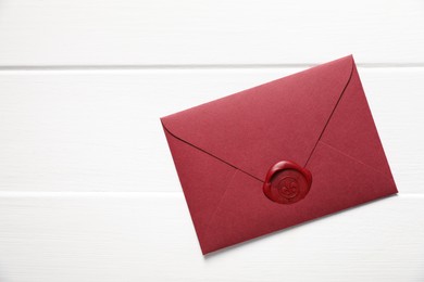 Photo of Envelope with wax seal on white wooden table, top view. Space for text