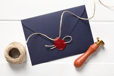 Photo of Envelope with wax seal, twine and stamp on white wooden table, flat lay